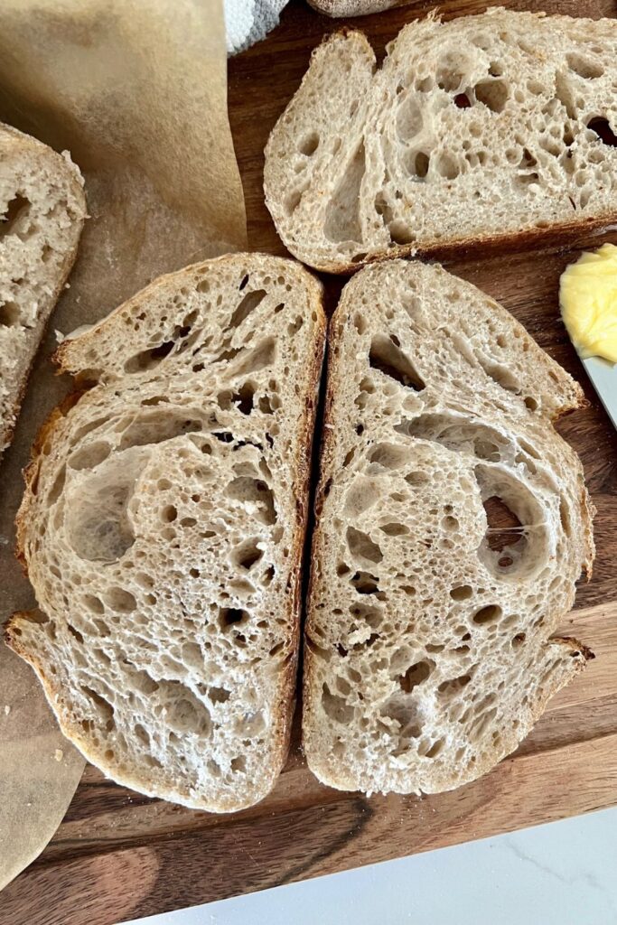 Two slices of rustic sourdough bread laying flat on a wooden board. The bread is positioned so that the base of each slice is touching each other.