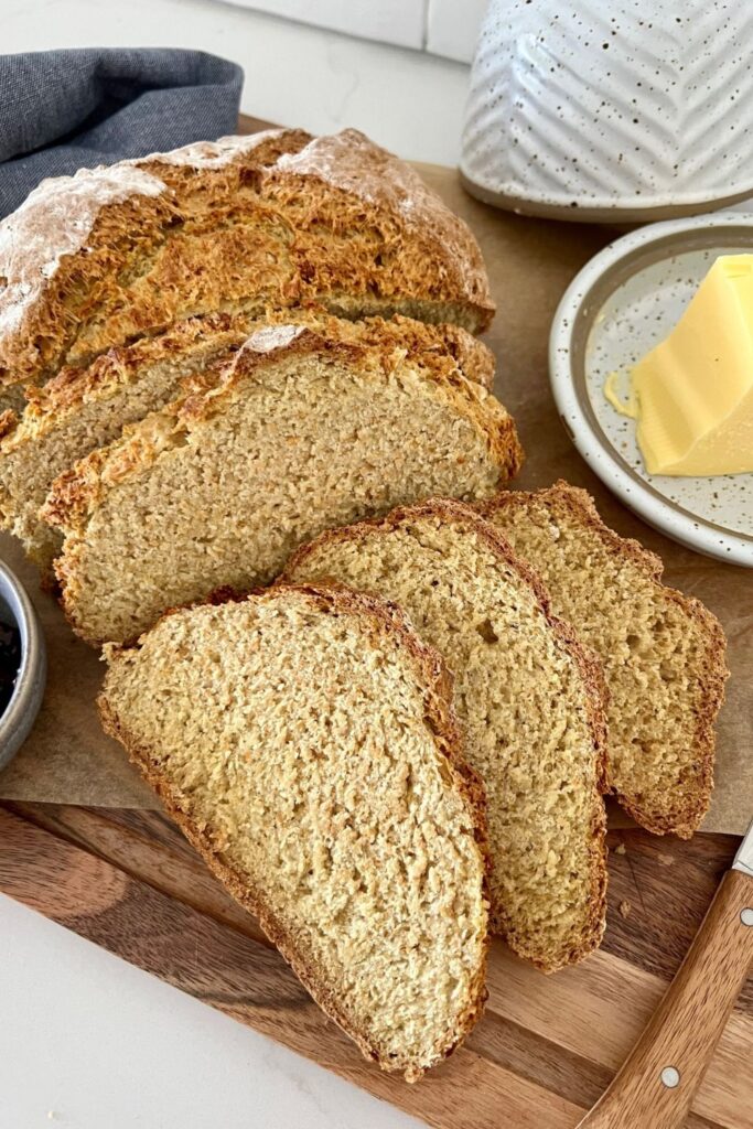 Four slices of Sourdough Irish Soda Bread sitting on a wooden board. There is a dish of butter to the right of the bread.