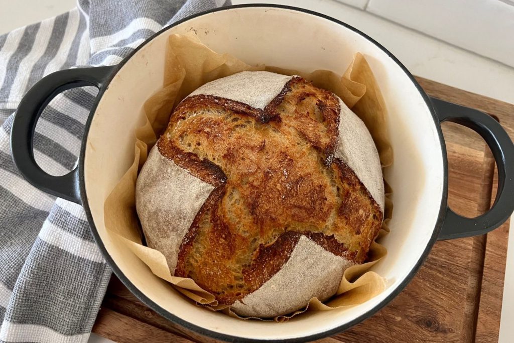 A sourdough rye bread boule sitting in a cream enamel Dutch Oven.
