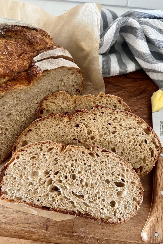 Slices of sourdough rye bread on a wooden board. There is a grey and white dish towel in the background.