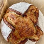 Sourdough rye bread recipe shaped into a boule. The bread has been scored with a cross and has been dusted with rye flour to enhance the scoring.