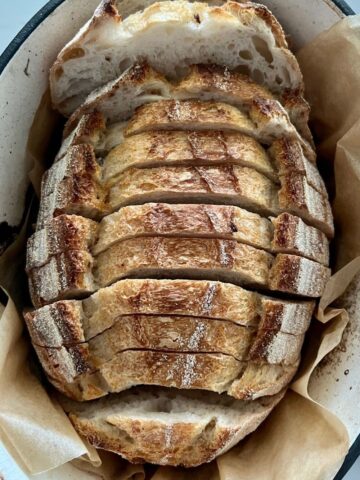 A loaf of overnight sourdough bread that has been sliced and then placed back into an enamel dutch oven.