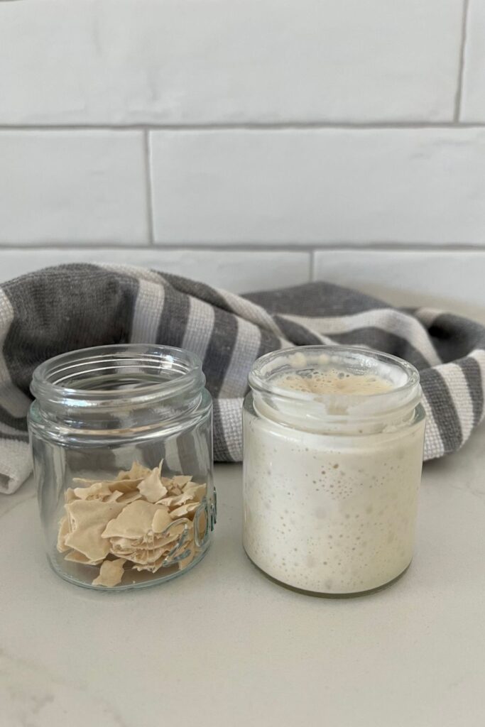 Two small jars of sourdough starter. The jar on the left is dried starter and the jar on the right is liquid starter. Neither jar has a lid on.