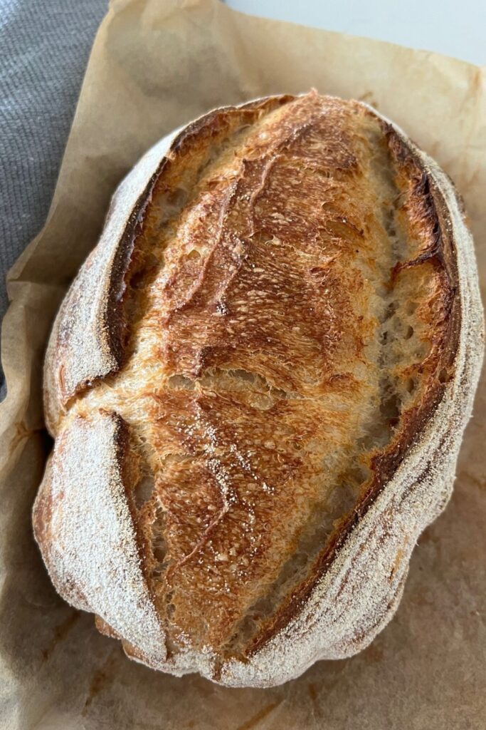 Loaf of sourdough bread sitting on a piece of parchment paper. The loaf of sourdough looks squashed and indented.