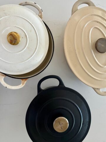 3 Dutch ovens for baking sourdough bread - a round cream enamel Dutch Oven with a brass knob, a black round enamel Dutch Oven with brass knob and a cream enamel Oval Dutch Oven, also with a brass knob.