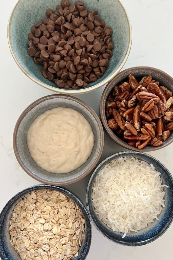 close up of the milk chocolate chips, pecans, shredded coconut, sourdough discard and rolled oats used in sourdough cowboy cookies.