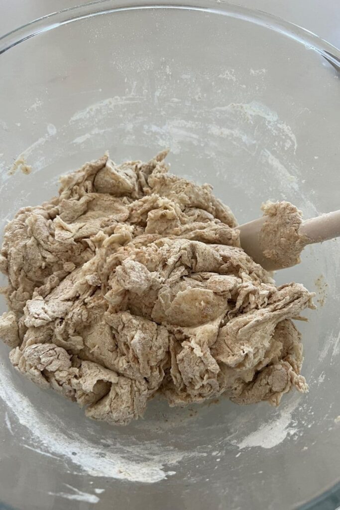 A bowl of shaggy sourdough dough that has just been mixed with a white jar spatula.