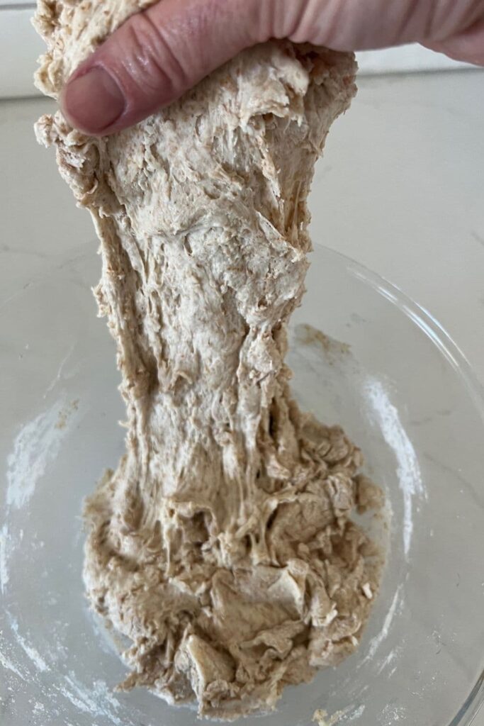 Spelt sourdough that is being pulled up from the bowl with one hand.