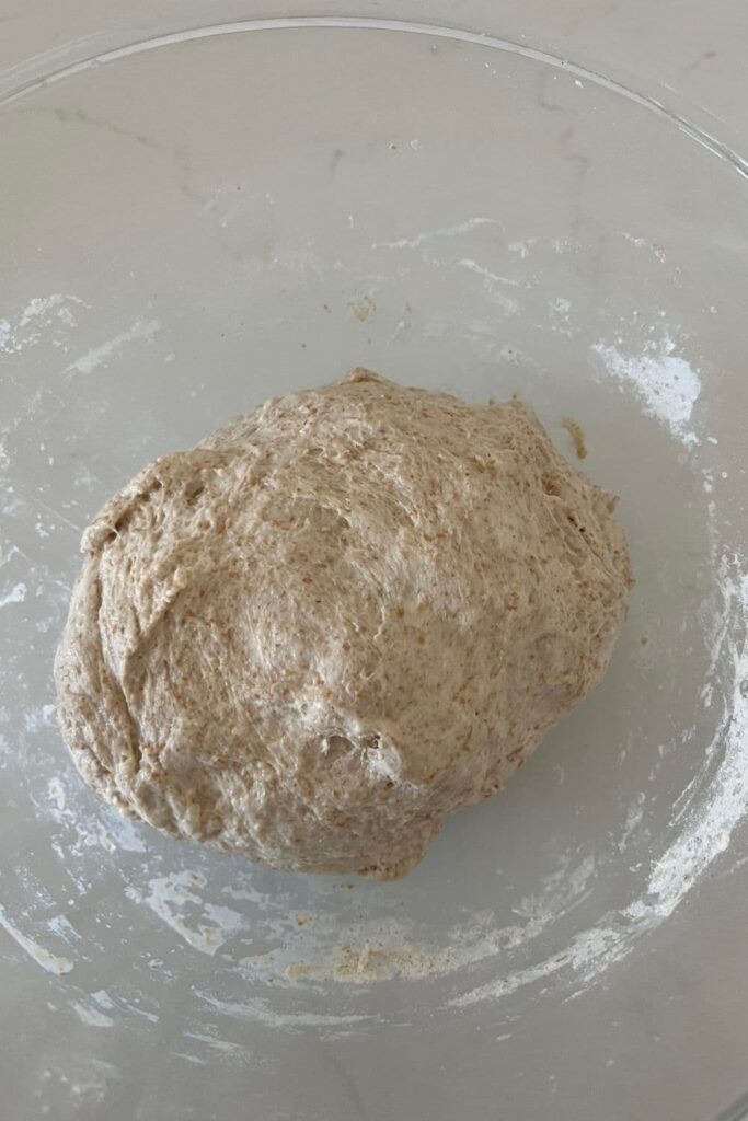 A glass bowl with a ball of spelt sourdough sitting in the middle. It has been formed into a ball after autolyse.