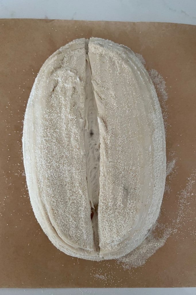 A loaf of roasted garlic sourdough bread that has been scored down the centre. The dough is unbaked and sitting on a piece of parchment paper.