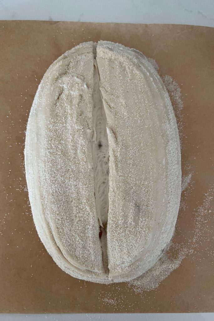 A loaf of roasted garlic sourdough bread that has been scored down the centre. The dough is unbaked and sitting on a piece of parchment paper.