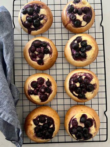 Sourdough brioche blueberry cheesecake rolls sitting on a wire rack with a blue dish towel sitting on the side.