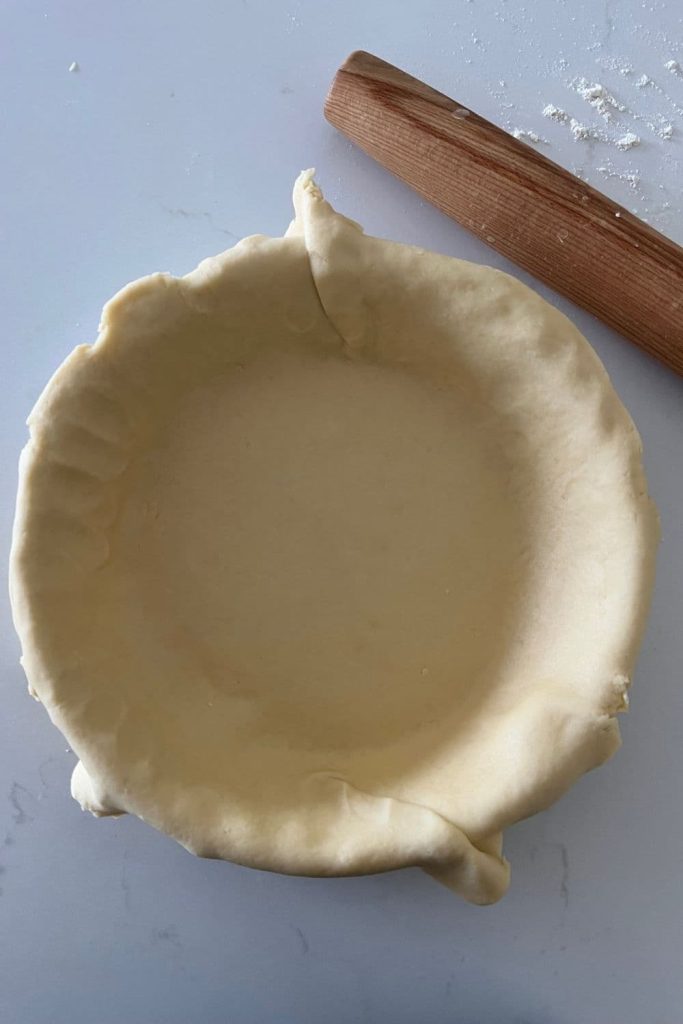 Sourdough pie crust that has been placed into a pie dish. There is a rolling pin to the right of the pie dish.