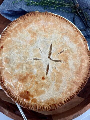 Sourdough chicken pot pie sitting in a wooden tray with a bunch of thyme next to it.