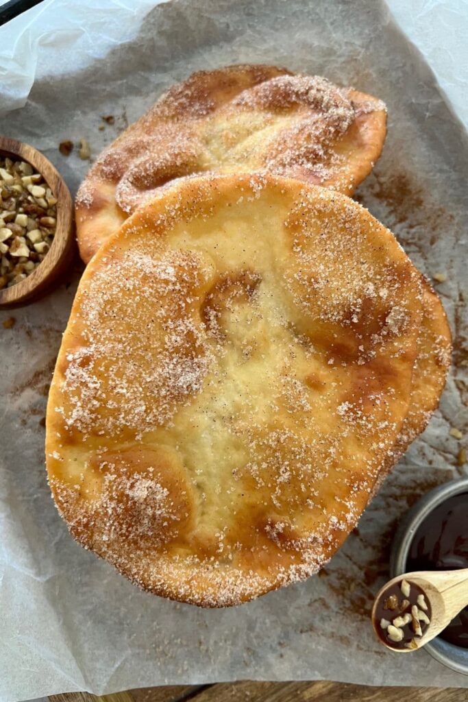 Two sourdough elephant ears sitting on a piece of greaseproof paper. They have been dusted with cinnamon sugar.