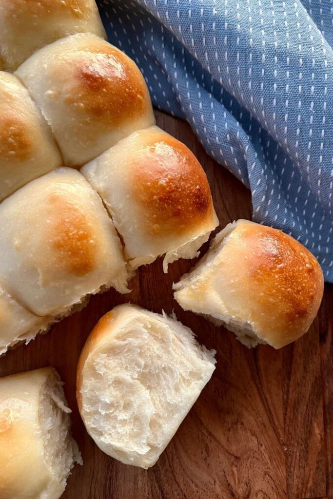 sourdough dinner rolls placed on a wooden board. One of the dinner rolls is tipped on its side so you can see the soft texture of the roll.