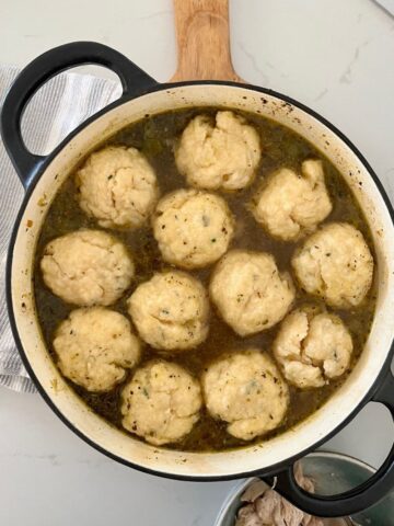 Black enamel Dutch Oven full of chicken soup with 12 sourdough dumplings floating on the top.