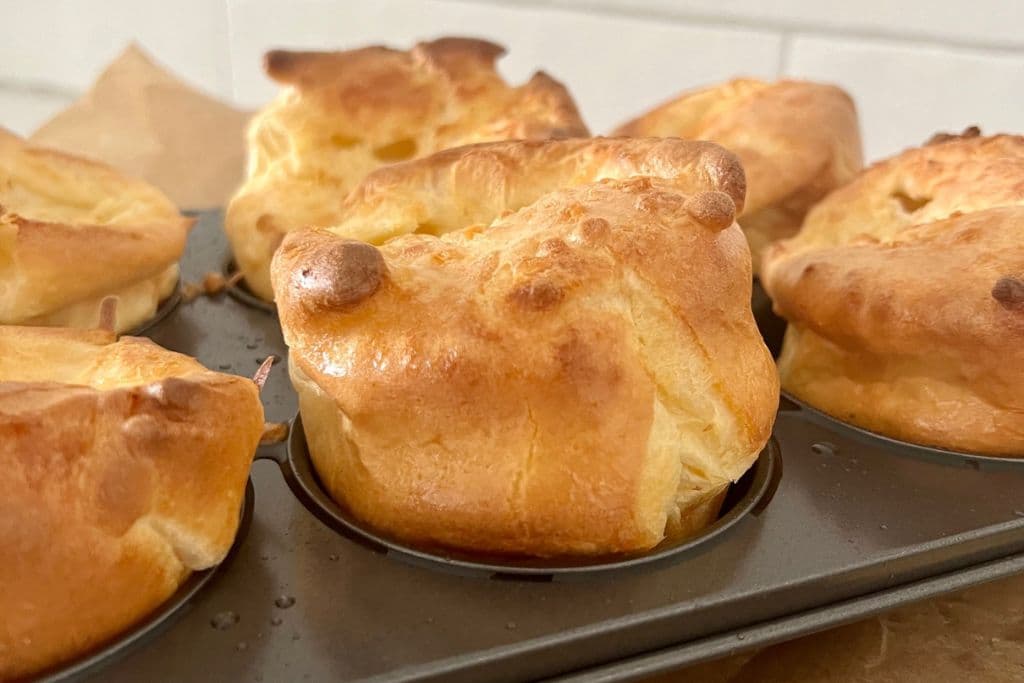 Sourdough popovers that have just come out of the oven. They are super puffy and sitting in a muffin tray.