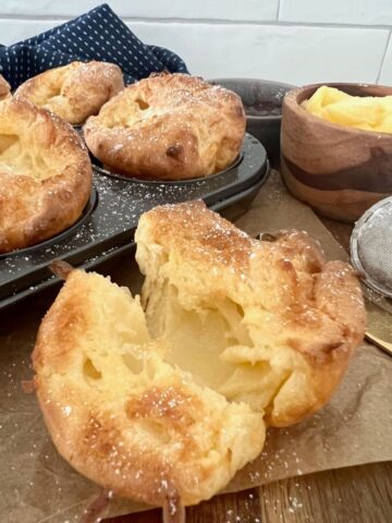 Sourdough popovers in a muffin pan. There is a sourdough popover up close that has been broken open to show the hollow interior.