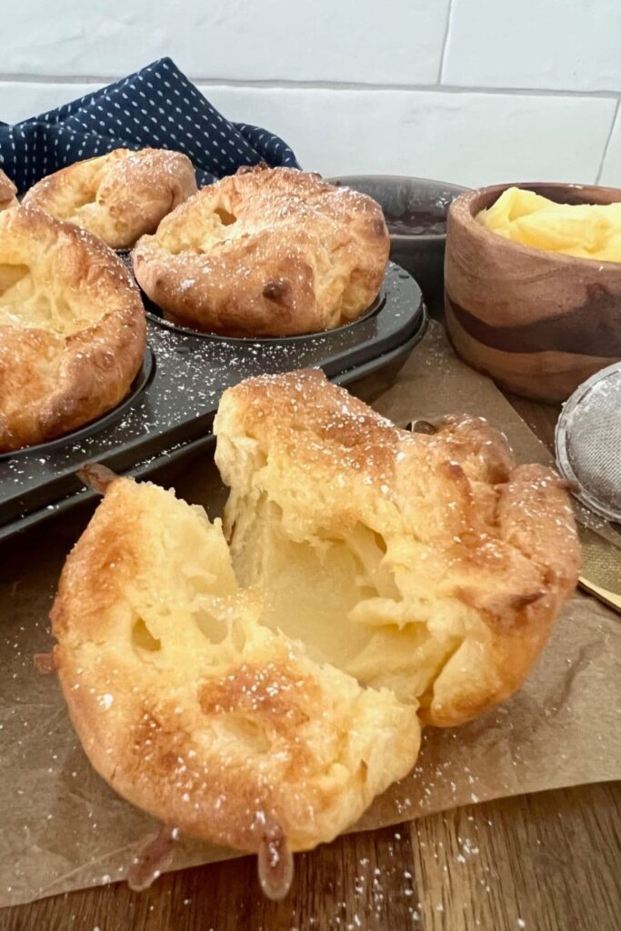 Sourdough popovers in a muffin pan. There is a sourdough popover up close that has been broken open to show the hollow interior.