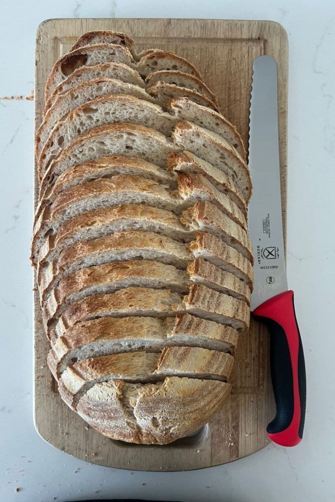 Loaf of sourdough bread that has been sliced using a Mercer 10" knife. The red handled serrated bread knife is sitting next to the loaf of bread.