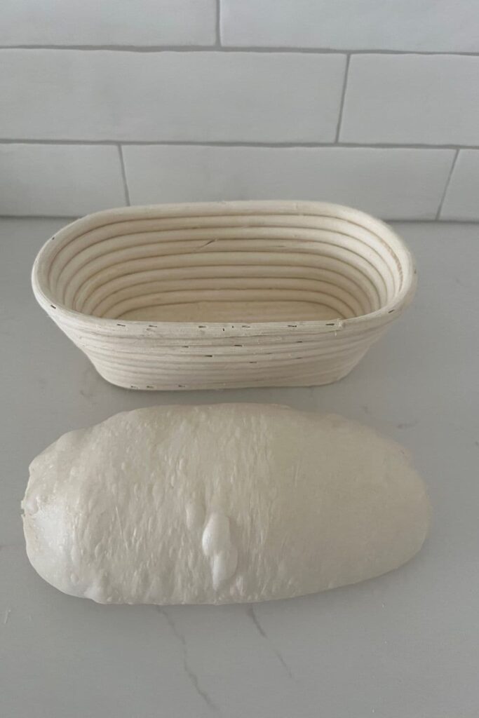 Sourdough that has been shaped into a batard. There is a banneton in the background of the photo.