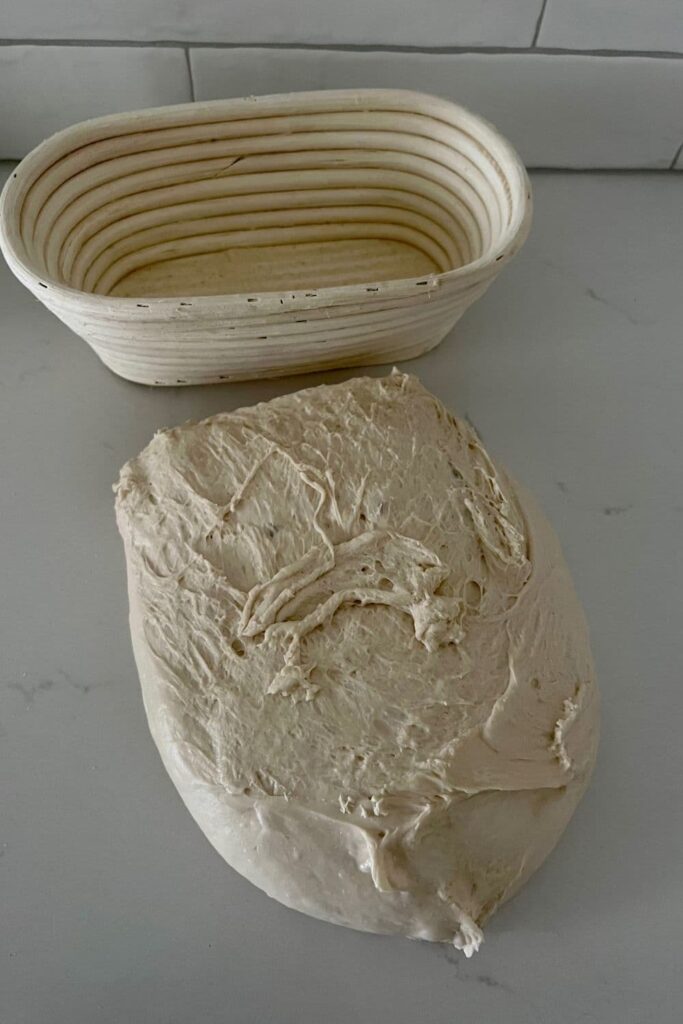 Sourdough that has been tipped out on the counter ready to shape. There is a banneton sitting in the background of the photo.