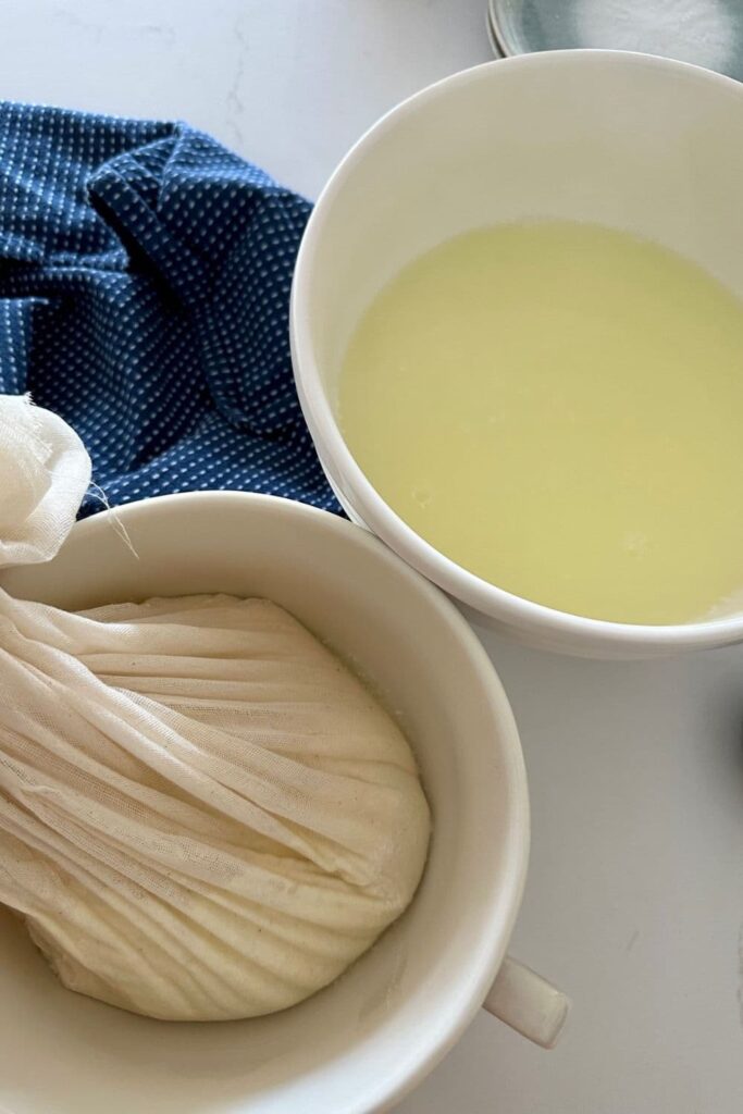 A bowl of ricotta whey sitting next to a dish of ricotta straining in some cheese cloth.