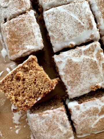 Sourdough Applesauce Cake covered in yogurt glaze and cinnamon. There is a piece of the cake that is laid on its side so you can see the texture.