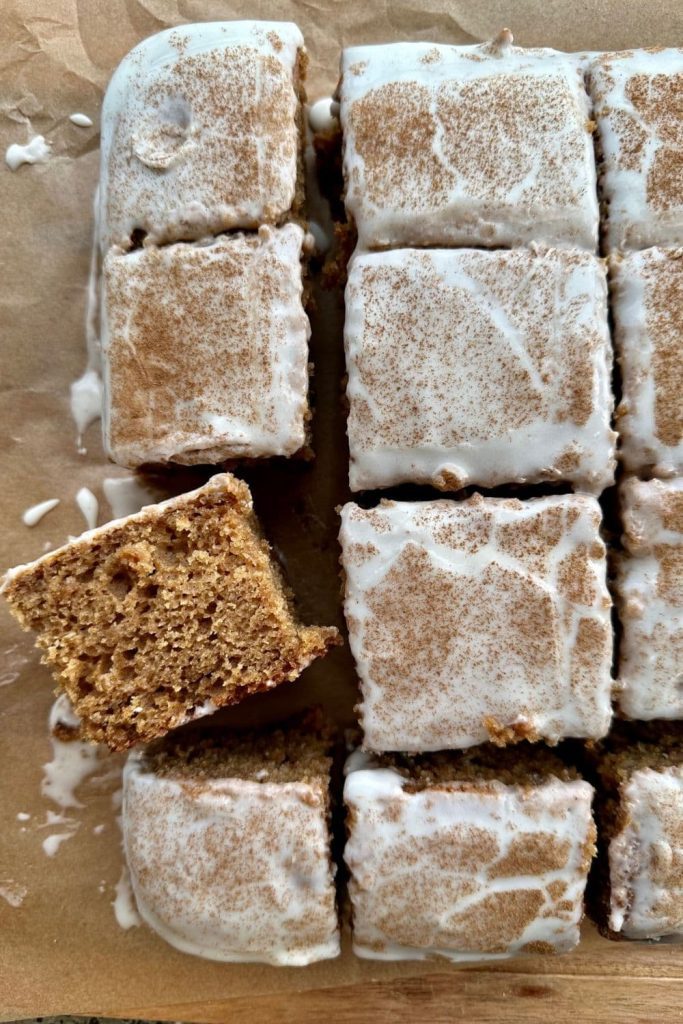Sourdough Applesauce Cake topped with sweet yogurt glaze and cut into squares. There is one square laying on it's side so you can see the moist texture of the cake.