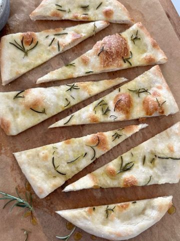 Sourdough pizza bianca sprinkled with rosemary and salt and sliced into wedges - served on a wooden board.