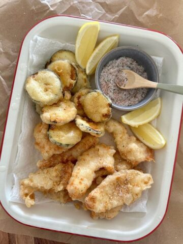 Cream enamel tray containing zucchini and chicken that has been lightly fried in sourdough discard batter. There are some lemon slices and a small dish of salt in the tray also.