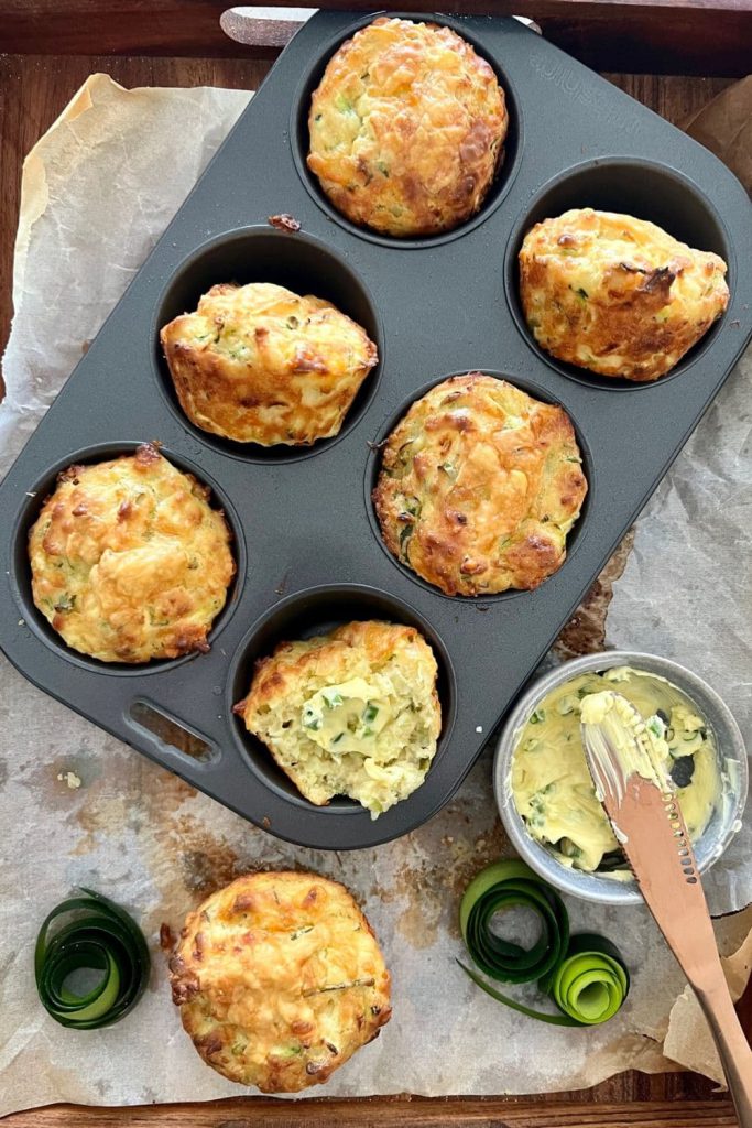 Sourdough zucchini muffins sitting in a 6 hole muffin tray next to a bowl of whipped herb butter - the ultimate sourdough snacks!