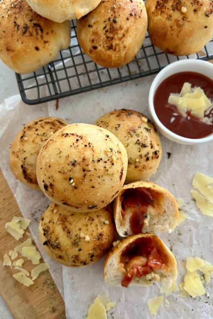 sourdough pizza pockets sitting on some parchment paper. One of the pockets has been cut open to show the pizza filling inside.