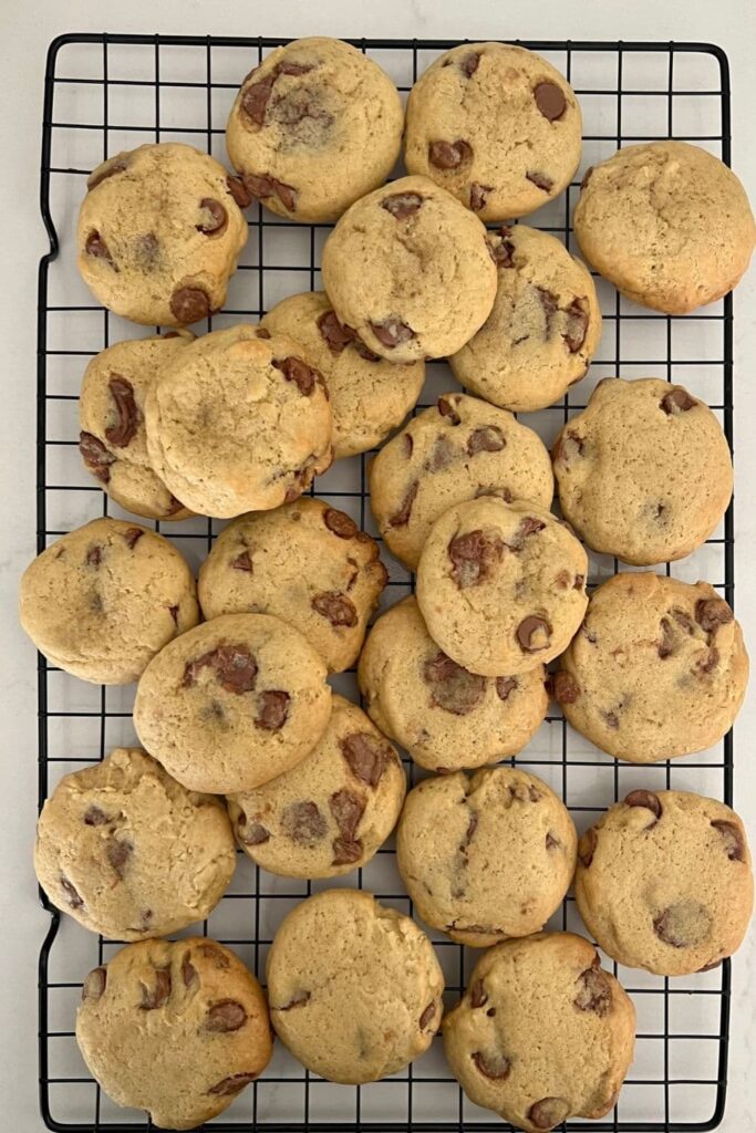 A pile of sourdough chocolate chip cookies sitting on a black wire cooking rack.