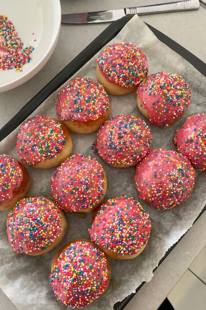 12 sourdough iced buns that have been iced with pink icing and sprinkles.