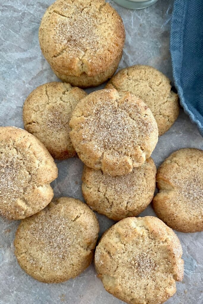 Sourdough snickerdoodles sitting on a piece of parchment paper. They are dusted in cinnamon sugar.