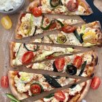 Sourdough Zucchini Pizza sliced into triangle wedges. This oval shaped pizza is topped with ricotta, zucchini ribbons and cherry tomatoes.