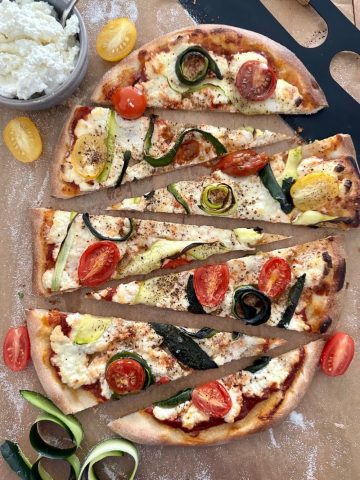 Sourdough Zucchini Pizza sliced into triangle wedges. This oval shaped pizza is topped with ricotta, zucchini ribbons and cherry tomatoes.