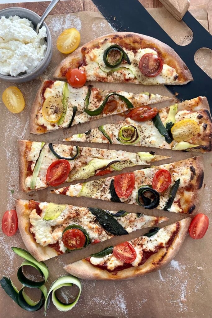 Sourdough Zucchini Pizza sliced into triangle wedges. This oval shaped pizza is topped with ricotta, zucchini ribbons and cherry tomatoes.