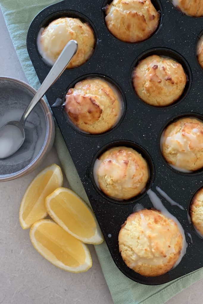 A tray of sourdough lemon muffins with some fresh lemons sitting next to the tray.
