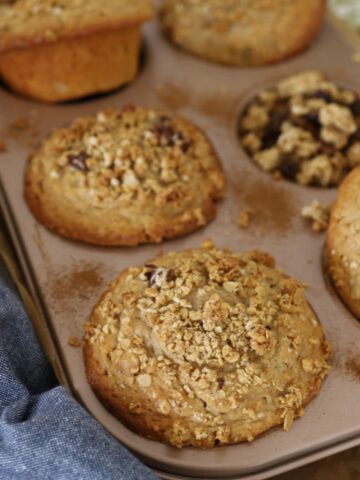 JUMBO SOURDOUGH GRANOLA MUFFINS - FEATURE IMAGE Sourdough Granola Muffins are sitting in a giant 6 hole muffin tin with a blue dish towel in the foreground.