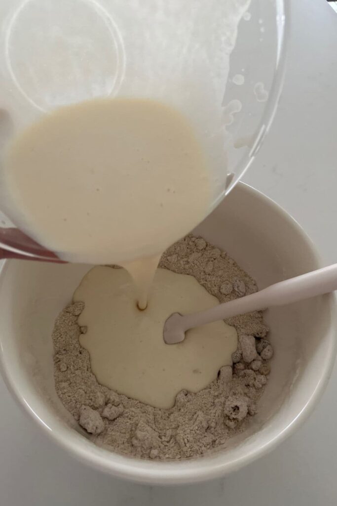 wet ingredients being poured into a bowl of dry ingredients to make sourdough granola muffins.