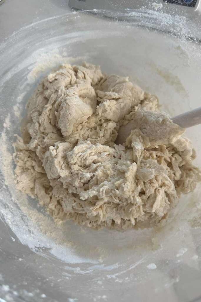 Shaggy dough sitting in a glass bowl with a white jar spatula.