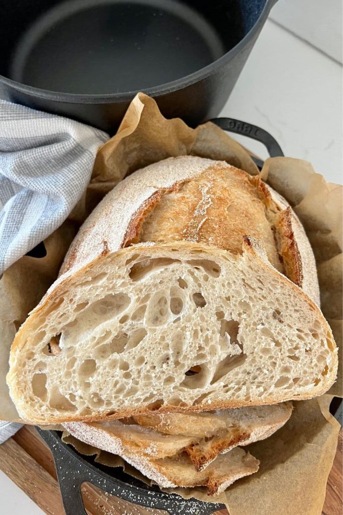 A slice of sourdough bread that has the perfect crumb. It is sitting on top of a loaf of sourdough bread.