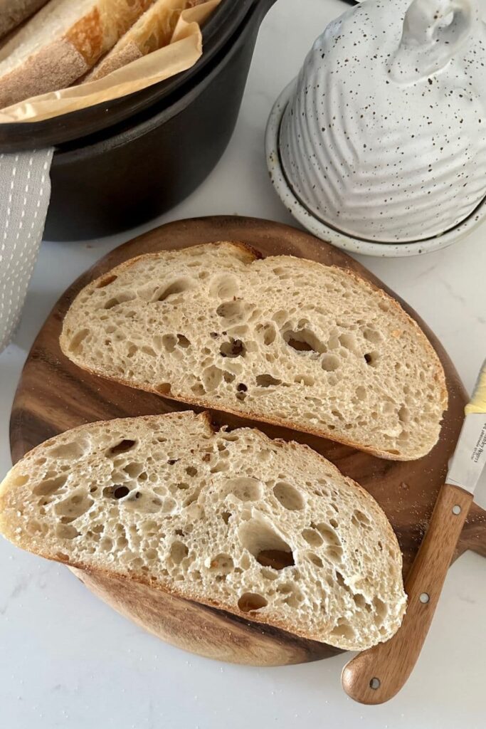 Sourdough bread made with all purpose flour. There are two slices laid on a round wooden board and you can see a butter dish in the top right corner of the photo.