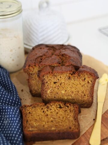 A loaf of sourdough discard pumpkin spice bread that has been sliced open and laid on a wooden board.