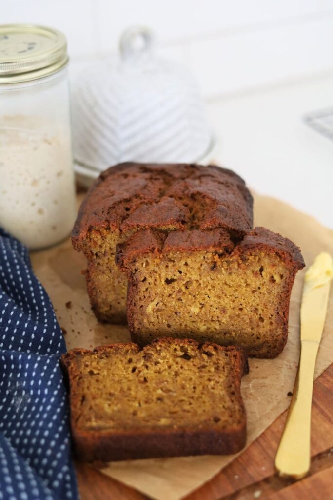 A loaf of sourdough discard pumpkin spice bread that has been sliced open and laid on a wooden board.