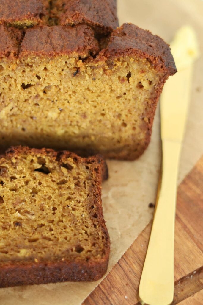 A loaf of sourdough discard pumpkin spice bread sitting next to a gold butter knife.