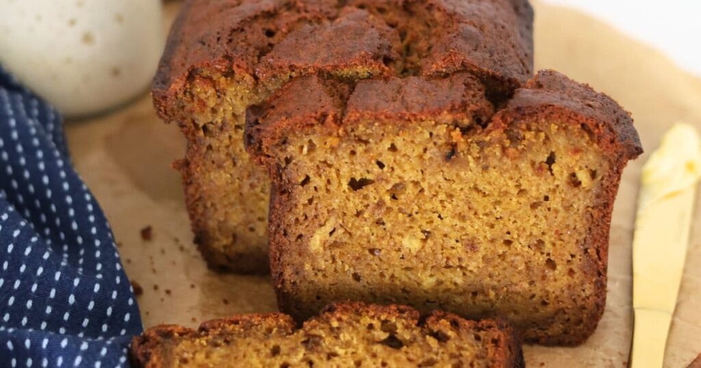 Sourdough discard pumpkin spice bread sliced and laid on a sheet of parchment paper. You can see a jar of sourdough starter in the background.